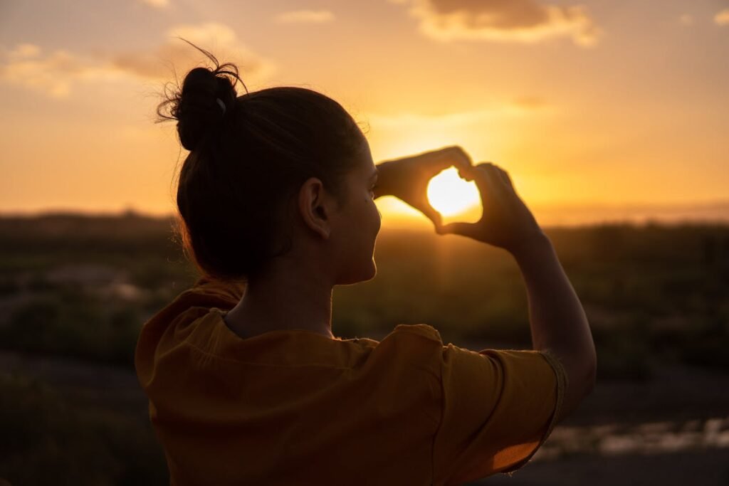 Mulher em frente ao pôr do sol formando um coração com as mãos, simbolizando amor-próprio e reconstrução da autoestima após um relacionamento tóxico.