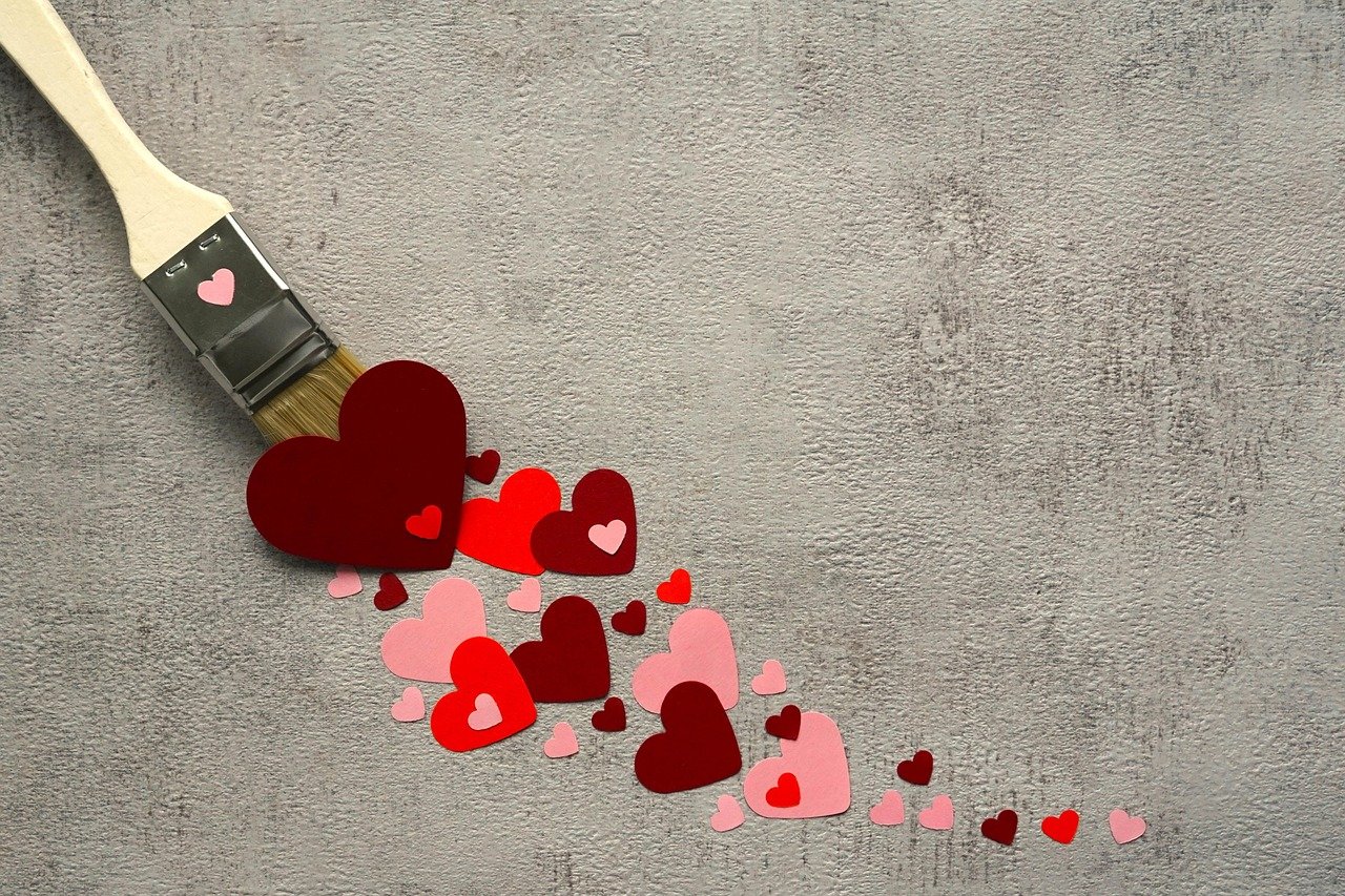 Pincel pintando vários corações em tons de vermelho e rosa, simbolizando o hábito de se apaixonar repetidamente por quem não retribui.
