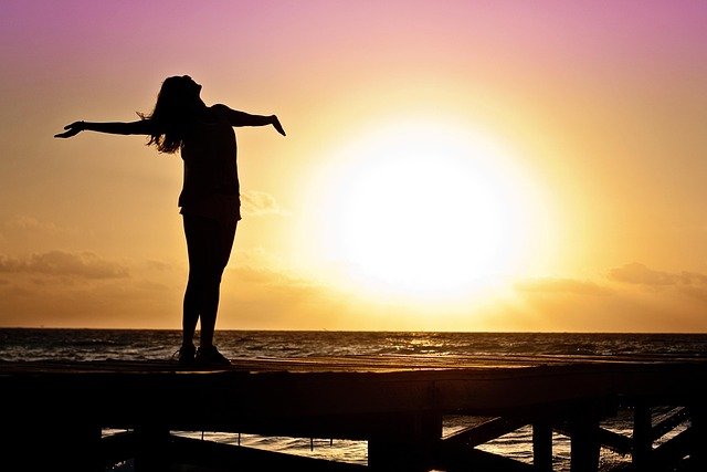 Mulher de braços abertos em frente ao pôr do sol, simbolizando liberdade, autoestima e recomeço emocional.