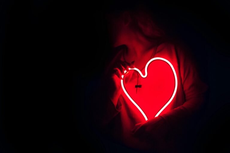 Mulher segurando um coração de neon vermelho no peito, simbolizando amor-próprio, cura emocional e reconexão com sua essência.