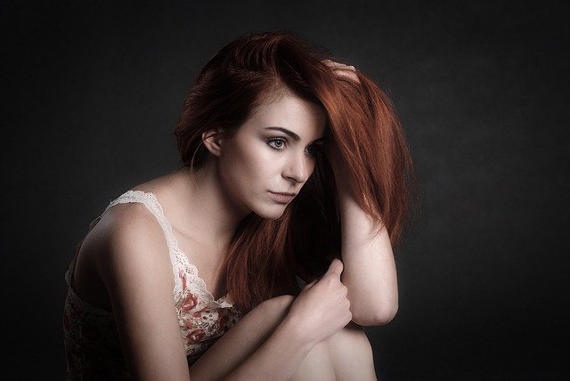 Mulher pensativa e triste, com expressão de luto emocional, sentada em um ambiente escuro.