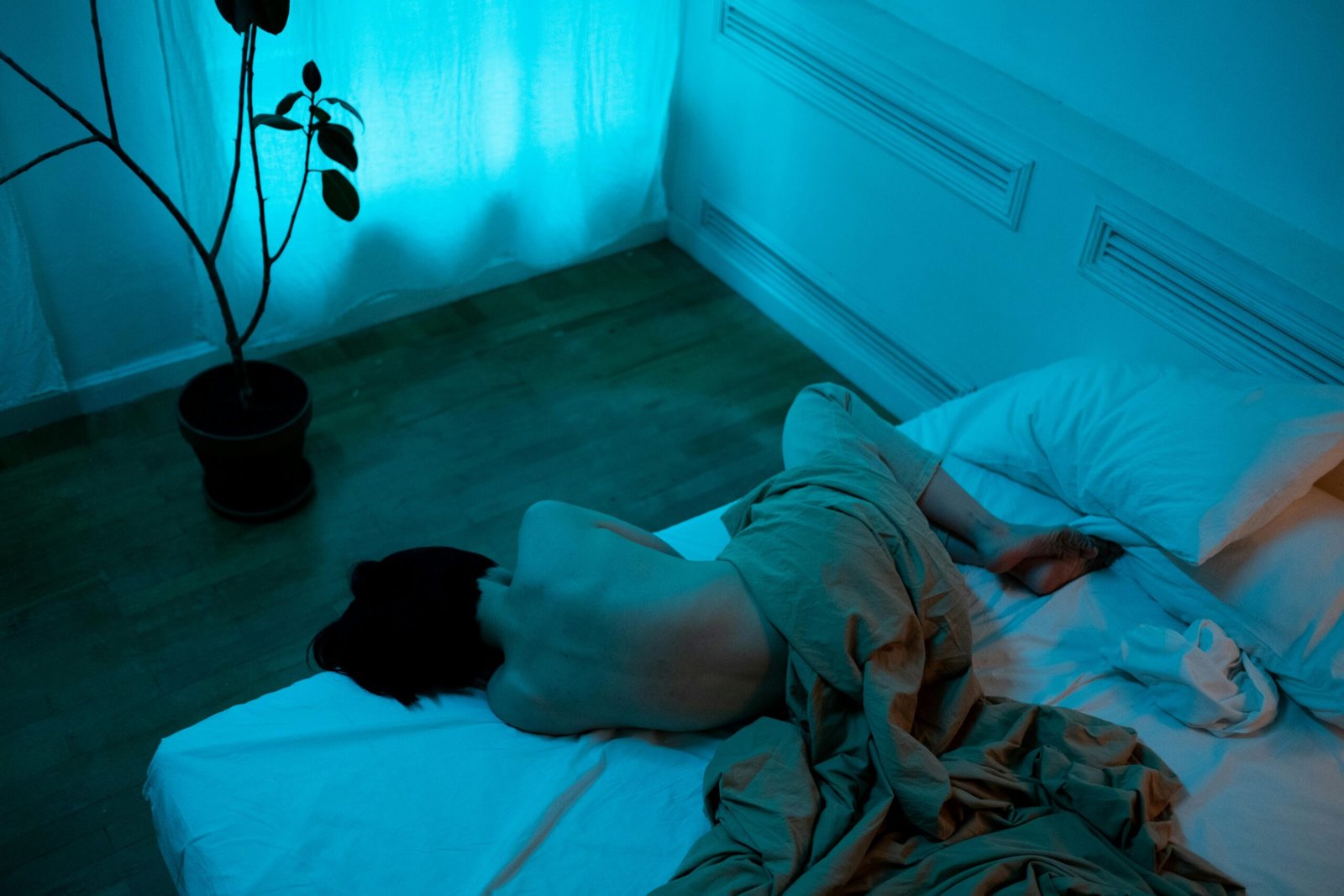 Mulher deitada na cama em um quarto escuro, cercada por luz azul, representando um momento de solidão e introspecção.